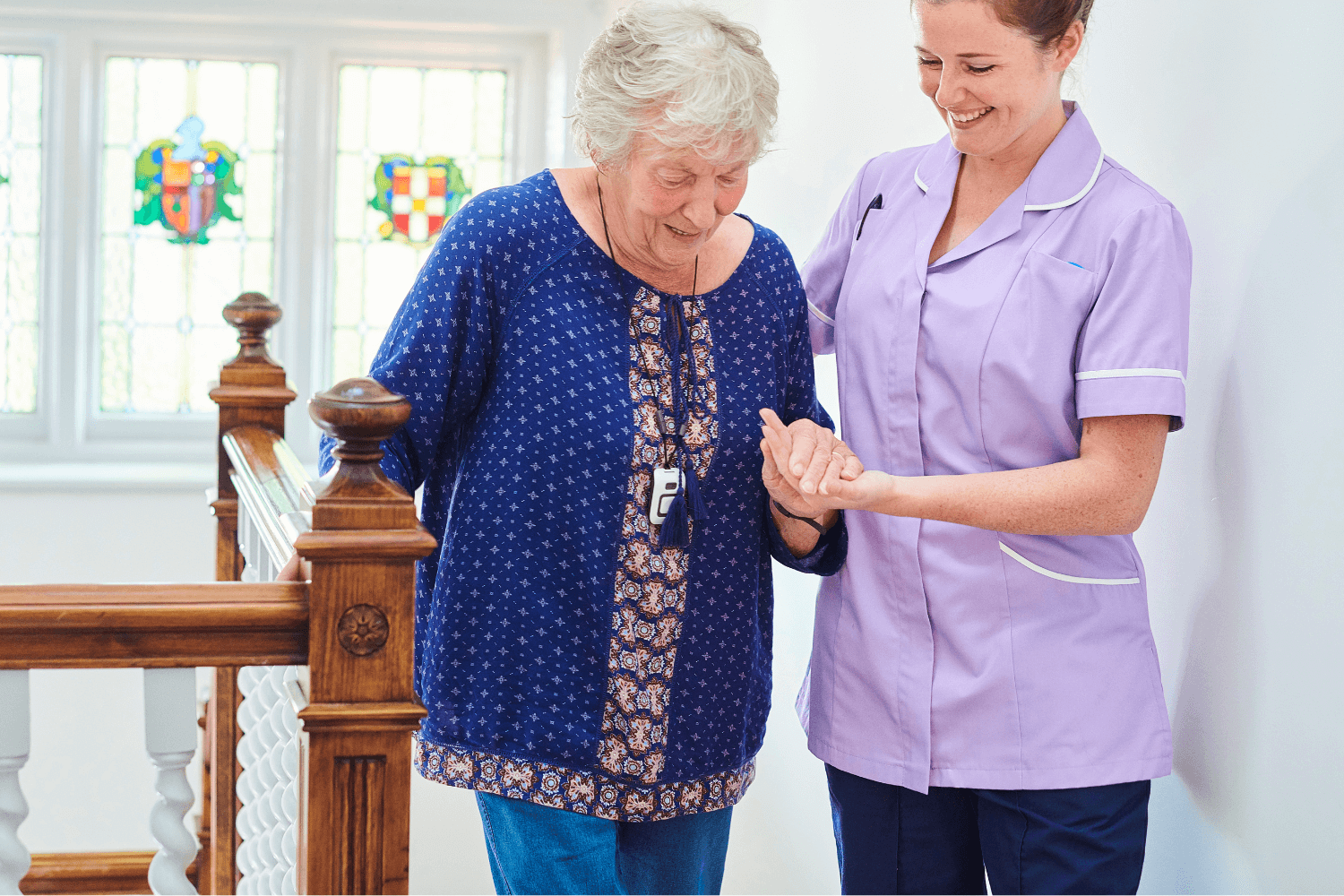 elderly lady held by a nurse in a purple shirt on the stairs